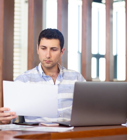 front-view-young-handsome-man-striped-shirt-working-inside-conference-hall-using-his-silver-laptop-looking-through-documents-daytime-work-activity-building_140725-15444